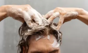 Manos con espuma masajean el cuero cabelludo, demostrando cómo lavarse el pelo correctamente para una limpieza profunda y un cabello saludable.