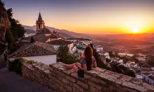 Una mujer contempla el atardecer sobre un pueblo blanco, con tejados de los mayses y montañas al fondo.