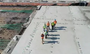 Grupa budowlańców na placu budowy, dyskutująca o cenie betonu i postępach prac. W tle zbrojenie i świeżo wylany beton.