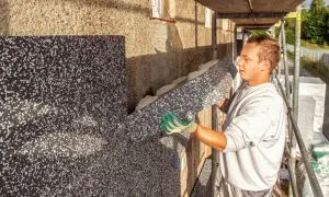 Pracownik montuje styropian na ścianie starego domu, zapobiegając wilgoci i poprawiając izolację.