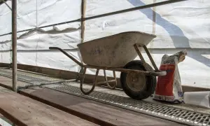 Wózek budowlany i worek z zaprawą na rusztowaniach. Budowa domu systemem gospodarczym to wyzwanie, ale też satysfakcja. Urząd skarbowy czeka na rozliczenie.