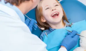 Uśmiechnięta dziewczynka u dentysty, która ma krzywy zgryz. Lekarz bada jej zęby.