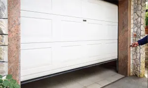 En person öppnar en vit garageport med fjärrkontroll. Garageport montering pågår.