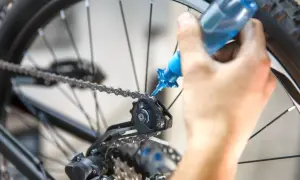 Dłoń aplikuje smar do łańcucha roweru. Płynny preparat zapewnia płynną jazdę, odpowiadając na pytanie: jaki smar do roweru wybrać.