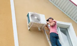 Técnico instala unidad exterior de aire acondicionado. Se aprecian las dimensiones de la unidad y el trabajo en la fachada.