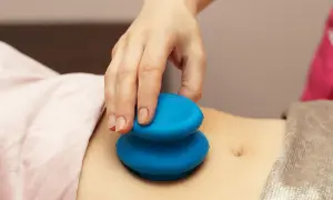 Dłoń terapeuty wykonuje masaż brzucha niebieskimi bańkami. Choć masaż bańką chińską efekty uboczne są rzadkie, warto znać potencjalne skutki.