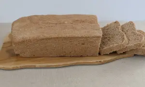 Bochenek chleba graham pokrojony na kromki, leżący na drewnianej desce.
