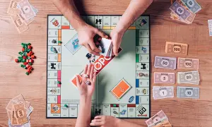 Ręce graczy dzielą pieniądze Monopoly na planszy gry, obok kostek i żetonów.