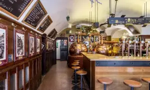 Interno di un locale tradizionale con alambicchi di rame, sgabelli e insegne che richiamano il mondo della birra e del **hopfen & co.**