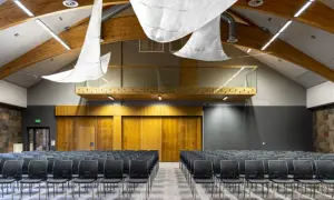 Nowoczesna sala konferencyjna z rzędami czarnych krzeseł, drewnianymi elementami i kamienną ścianą. Idealne miejsce na konferencje na Mazurach.