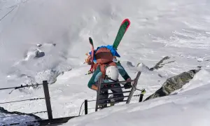 Escalade d'une échelle sur un flanc de montagne enneigé, skis sur le dos. L'ascension vers un sommet 4000 des Alpes, une aventure pas si facile.