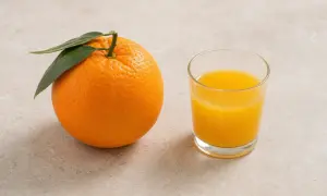 Arancia fresca con foglie verdi accanto a un bicchiere di spremuta d'arancia.