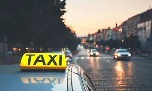 Żółty znak TAXI na dachu samochodu na tle miasta o zachodzie słońca.