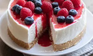 Cheesecake invitante con frutti di bosco freschi e salsa rossa. Una fetta è stata tolta, rivelando la sua consistenza cremosa.