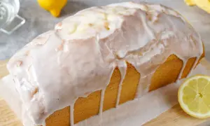 Ein saftiger Zitronenkuchen in Kastenform, überzogen mit süßem Zuckerguss. Ein Zitronenstück liegt daneben.