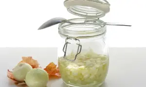 Słoik z domowym syropem z cebuli, obok dwie cebule i łuski. Łyżeczka oparta o słoik.