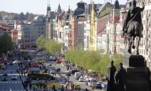 Pomnik konny na placu Wacława w Pradze, z widokiem na tętniącą życiem ulicę pełną ludzi i samochodów.