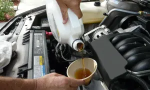 Händer häller ny olja i en bilmotor. För att veta hur ofta byta oljefilter, kolla bilens manual.