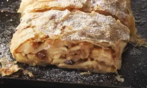 Ein saftiger Apfelstrudel, bestäubt mit Puderzucker, wartet darauf, nach diesem Apfelstrudel Rezept zubereitet zu werden.