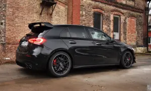 Czarny Mercedes-AMG A45s z masywnym spojlerem i czerwonymi zaciskami hamulcowymi stoi na mokrej nawierzchni przed starą ceglaną kamienicą.