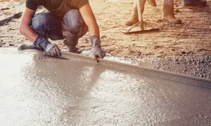 Pracownik wyrównuje świeżą wylewkę betonową na ziemi za pomocą łaty. To kluczowy etap, jak zrobić wylewkę betonową na ziemi.
