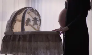 Gravid kvinna med ruckbart huvud vid en vagga med nallar.