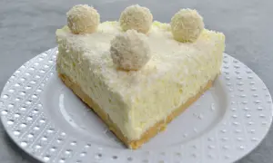 Pyszny sernik Rafaello, udekorowany wiórkami kokosowymi i kulkami przypominającymi Rafaello.