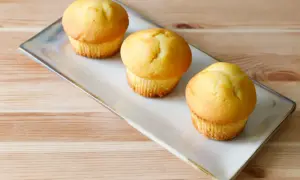 Tre soffici muffin allo yogurt dorati, serviti su un piatto rettangolare su un tavolo di legno.