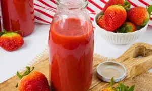 Frische Erdbeeren werden zu einem leckeren Smoothie verarbeitet. Eine Flasche mit dem roten Fruchtgetränk steht bereit.