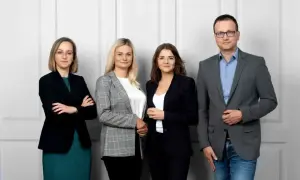 Cztery osoby w strojach biznesowych stoją przed jasną ścianą.
