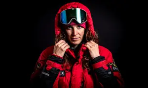 Tamara Lunger, bereit für extreme Bedingungen, zieht ihre rote Kapuze hoch. Ihre Skibrille spiegelt das Licht.