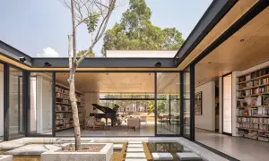 Modernas casas con patio interior central, un árbol solitario y un estanque de agua reflejan la luz natural.