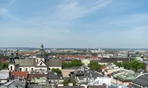 Widok na krakowskie dachy i kościół z kopułą. W tle nowoczesne budynki, które mogą wpływać na ceny mieszkań w Krakowie za m2.