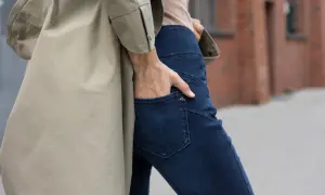 Kobieta w beżowym płaszczu i granatowych jeansach bootcut, które delikatnie rozszerzają się ku dołowi.