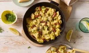 Pyszne tortellini grzybowe w kremowym sosie, posypane parmezanem i boczkiem, podane z cytryną i koperkiem.