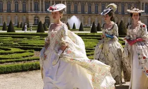 Kvinnor i magnifika **rococo fashion**-klänningar med blomstermönster promenerar i en formell trädgård framför ett palats.