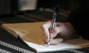 Mano che scrive su un quaderno, un momento intimo che ricorda l'apertura di un testamento olografo.