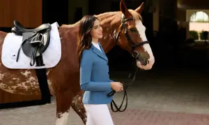 Elegancka amazonka w niebieskiej marynarce prowadzi konia w siodle. Wodze Thiedemanna pewnie trzyma w dłoni.