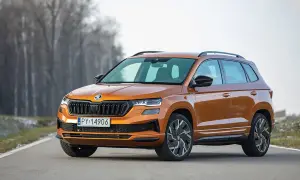 Pomarańczowy Skoda Karoq Sportline na drodze, z drzewami w tle.