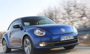 Niebieski, nowy Beetle pędzi po drodze, za nim rozmyty krajobraz drzew.
