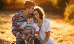 Ciepłe, złote światło otula rodzinę podczas sesji rodzinnych. Tata całuje główkę dziecka, mama uśmiecha się, wtulona w męża.