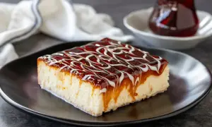 Una fetta di torta trilece ricetta, bagnata da sciroppo e caramello, su piatto nero.