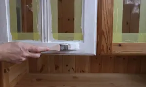 En hand målar en vit kant på en trämöbel. Maskeringstejp skyddar träet.