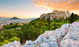 Akropolis reser sig över Aten, greklands huvudstad, med en dramatisk solnedgång i bakgrunden.