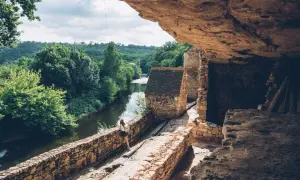 Une femme explore un village troglodytique en Dordogne, au bord d'une rivière paisible. Une belle idée de que faire en Dordogne.