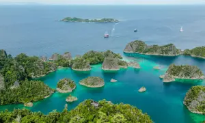 Traumhafte Anreise nach Raja Ampat: türkisfarbene Lagunen, grüne Inseln und Segelschiffe im azurblauen Meer.