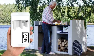 Man förbereder mat vid en murad grillplats vid en sjö. En mobil visar en 3D-modell av grillplatsen i AR.