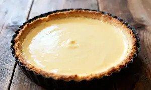 Un flan pâtissier grand-mère tout juste sorti du four, sa crème onctueuse et sa pâte dorée sur fond de bois rustique.
