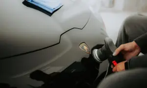 Ręka z polerką samochodową przy logo Lamborghini na czarnym lakierze.