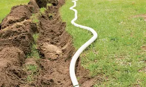 Ein Graben wird für das Erdkabel verlegen vorbereitet. Ein weißes Kabel schlängelt sich über das Gras neben dem aufgeworfenen Erdreich.